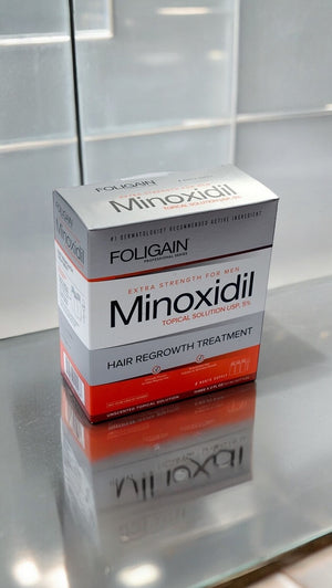 FOLIGAIN մինօքսիդիլի 5% տեղային լուծույթի տուփը՝ արտացոլող մակերեսի վրա։
